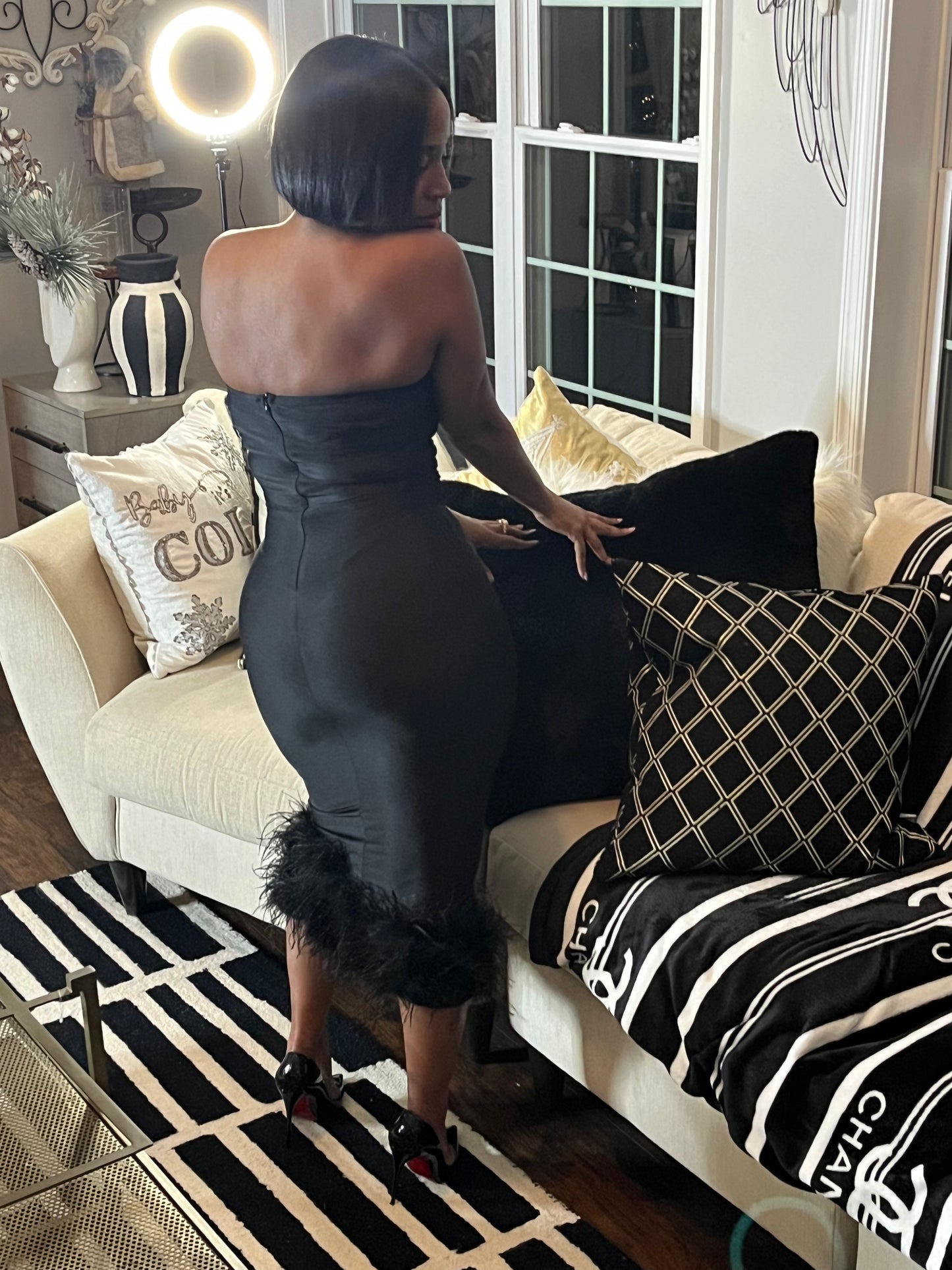Woman modeling back of black fitted dress with feather detail on the bottom