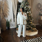 Woman standing in front of Christmas tree with white wide legged pants and jacket