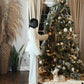 Woman touching ornament on Christmas tree while dressed in wide leg white pants and white jacket